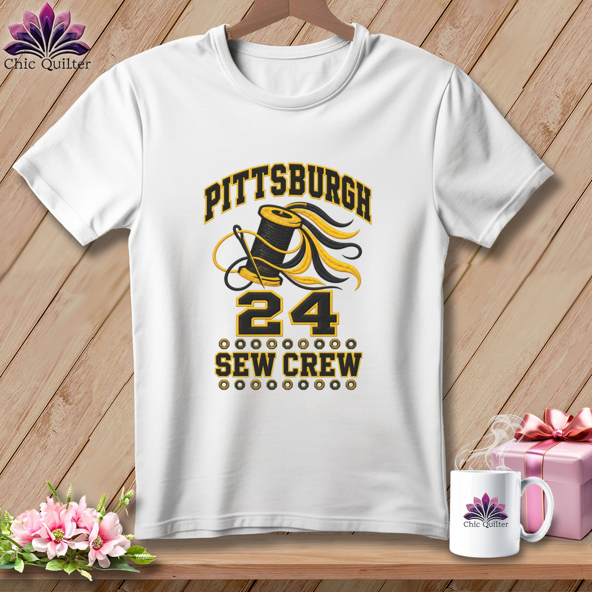 A white t-shirt hanging on a wooden background features a black and yellow graphic with text reading Pittsburgh 24 Sew Crew.