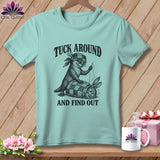 Light blue t-shirt featuring an otter sewing a quilt wrapped around a startled rabbit, with text reading TUCK AROUND AND FIND OUT.