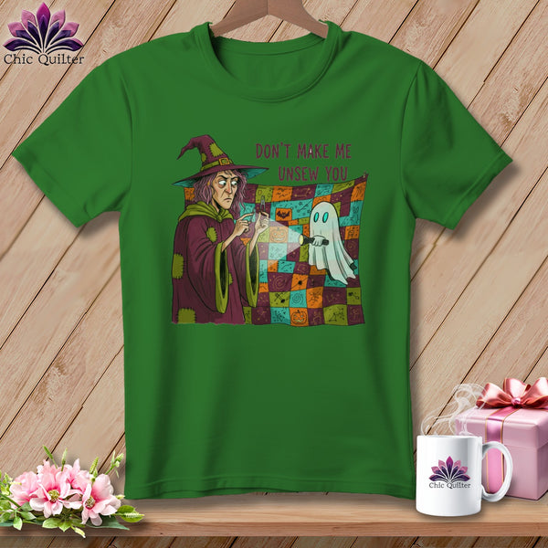 Green t-shirt with a witch and ghost sewing a Halloween-themed quilt.