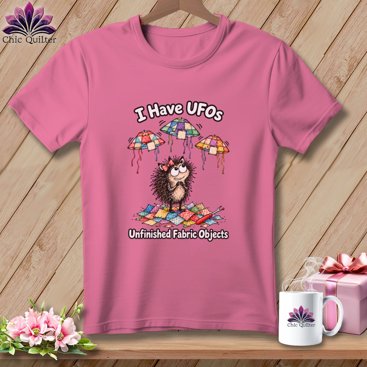 Pink t-shirt featuring a cartoon hedgehog, floating quilted UFOs, and the text I Have UFOs Unfinished Fabric Objects.