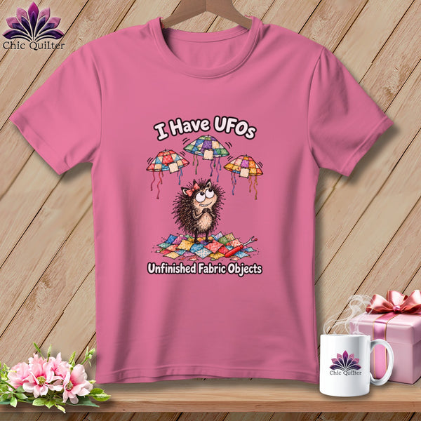 Pink t-shirt featuring a cartoon hedgehog, floating quilted UFOs, and the text I Have UFOs Unfinished Fabric Objects.