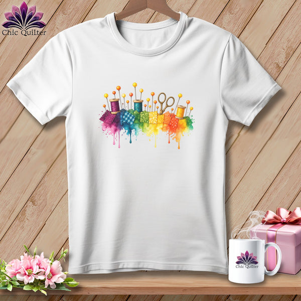 White t-shirt with watercolor sewing supplies and fabric scraps in rainbow colors.
