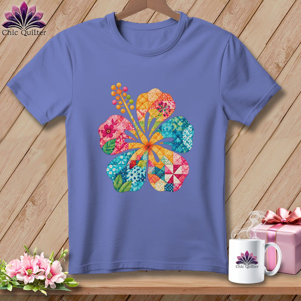 Periwinkle t-shirt on a wooden background, featuring a colorful patchwork hibiscus flower graphic on the chest.