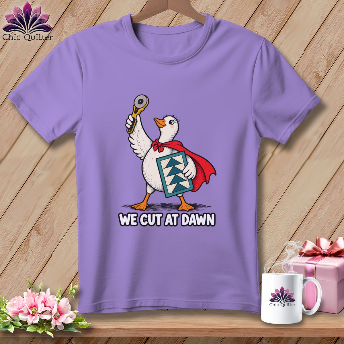 Light purple t-shirt featuring a cartoon duck holding a rotary cutter and text reading WE CUT AT DAWN.