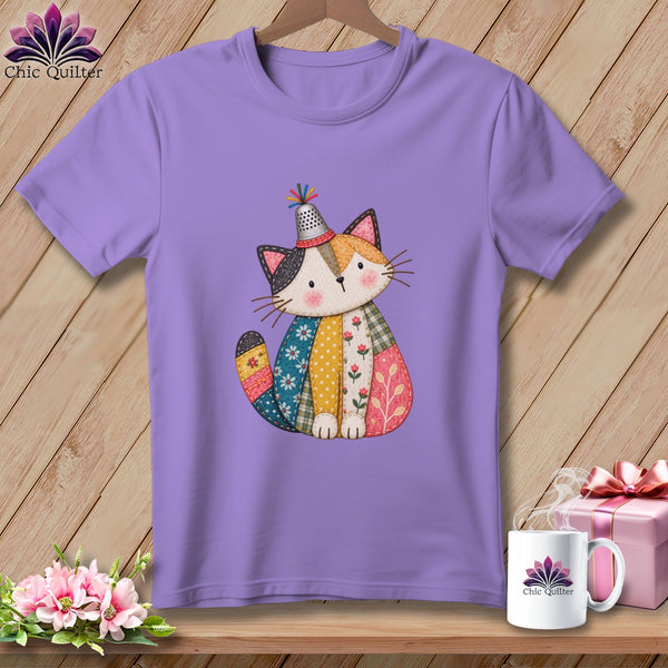 Purple short-sleeved t-shirt hanging on a wooden wall, featuring a patchwork cat graphic wearing a thimble hat.