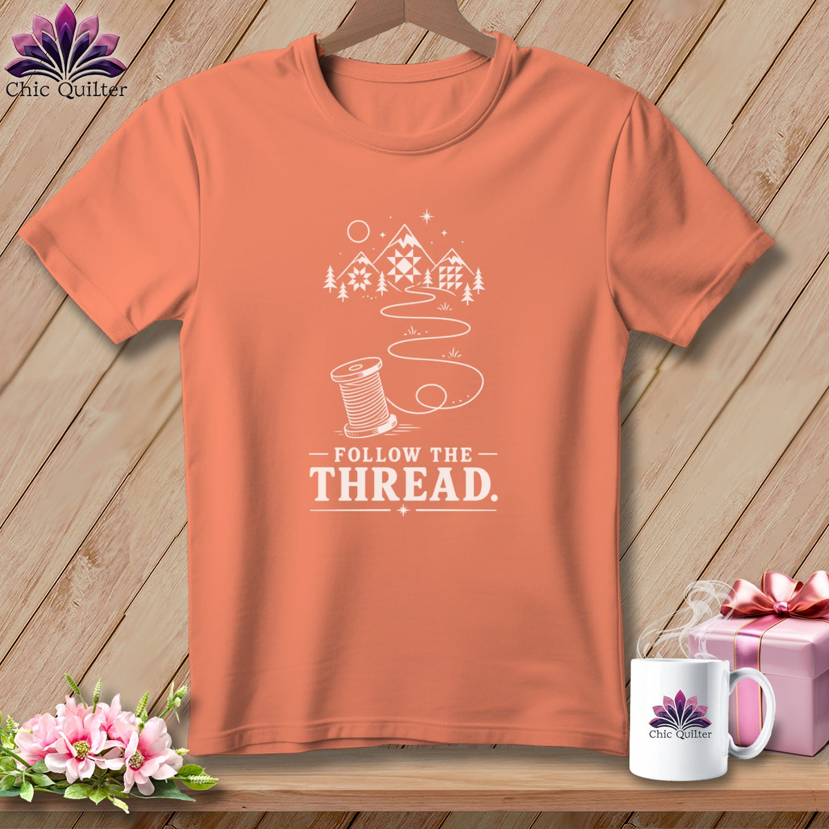 Orange t-shirt with white "Follow the Thread" text, spool, mountains, and trees graphic.