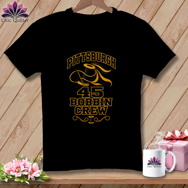 Black t-shirt featuring a yellow graphic of a spool of thread, needle, and text reading Pittsburgh Bobbin Crew.