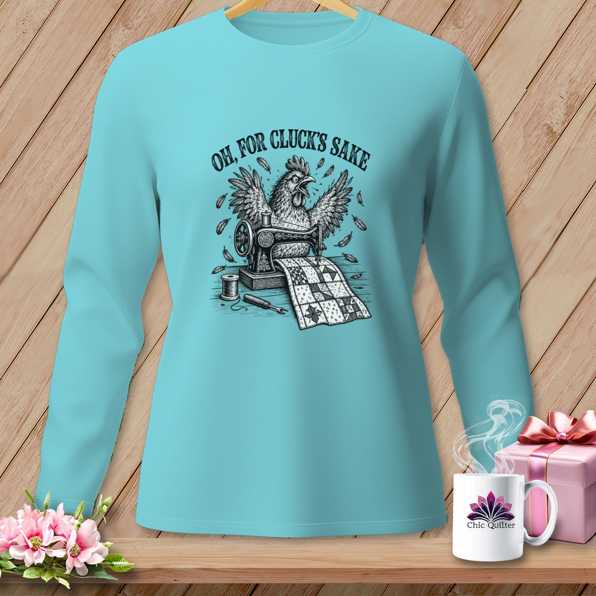 Long-sleeve turquoise shirt with a chicken sewing a quilt graphic and text "Oh, for cluck's sake".