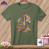 An olive green t-shirt features a colorful graphic of patchwork giraffes, folded fabrics, and quilting tools.