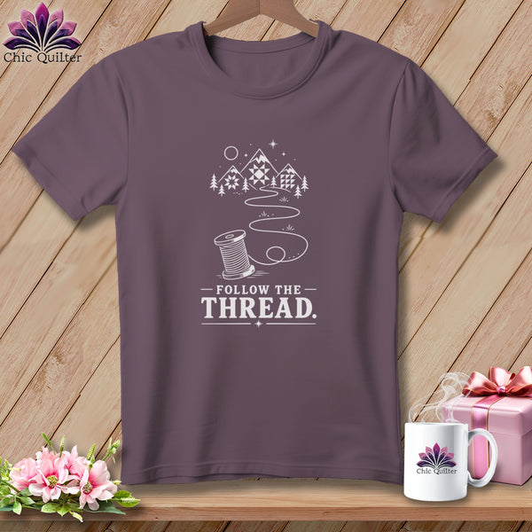 Purple t-shirt with "Follow the Thread" text, spool, mountains, and quilt designs.