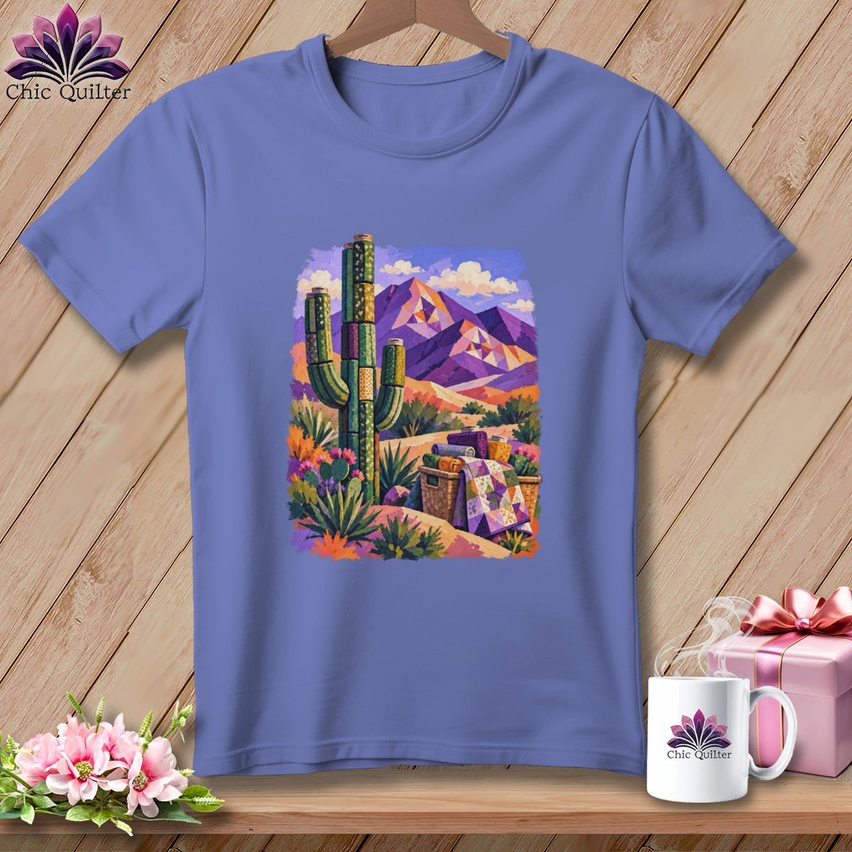 A periwinkle t-shirt on a wooden hanger, featuring a colorful desert landscape graphic with cacti, mountains, and a patterned quilt.