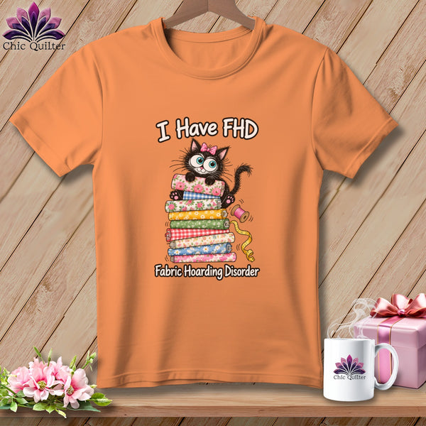 Orange t-shirt featuring a cartoon black cat with a pink bow sitting atop a stack of patterned fabric rolls and text reading I Have FHD Fabric Hoarding Disorder.
