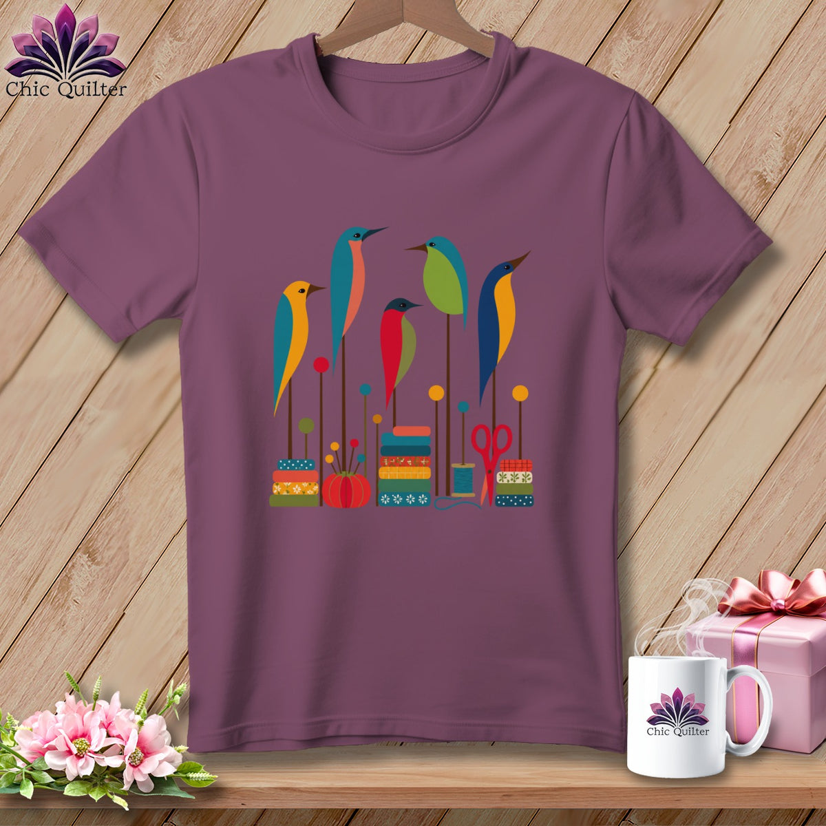 Plum crewneck t-shirt featuring a colorful graphic of five stylized birds perched on sewing-themed elements.