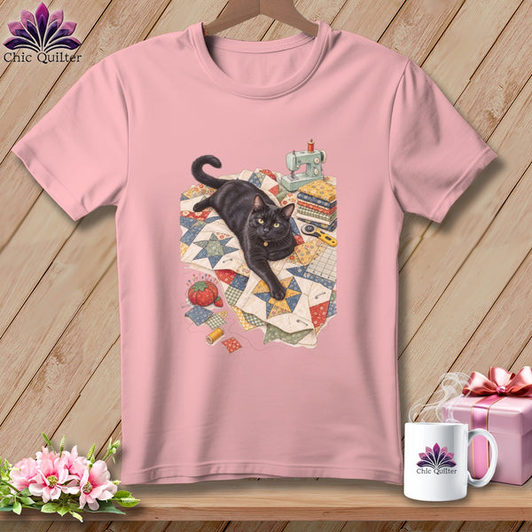 Pink t-shirt with a black cat on a quilt with sewing supplies.