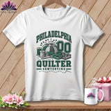 A white t-shirt hanging on a wooden background, featuring green text reading Philadelphia Quilter.