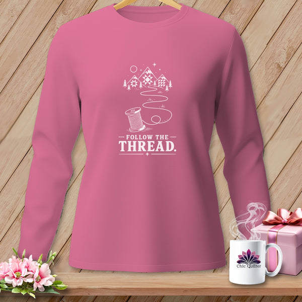 Pink long-sleeve shirt with white graphic of mountains, spool, and text "Follow the Thread."