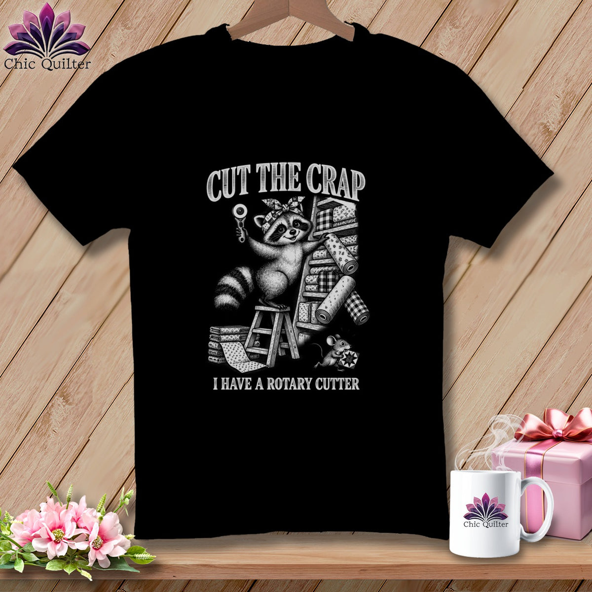 Black t-shirt with a raccoon holding a rotary cutter and fabric rolls.