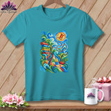 A teal t-shirt featuring a colorful graphic of quilting supplies, including fabric rolls, a needle, and thread.