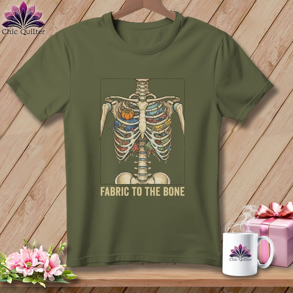 Olive green t-shirt with skeleton filled with fabric and scissors, text reads "FABRIC TO THE BONE."