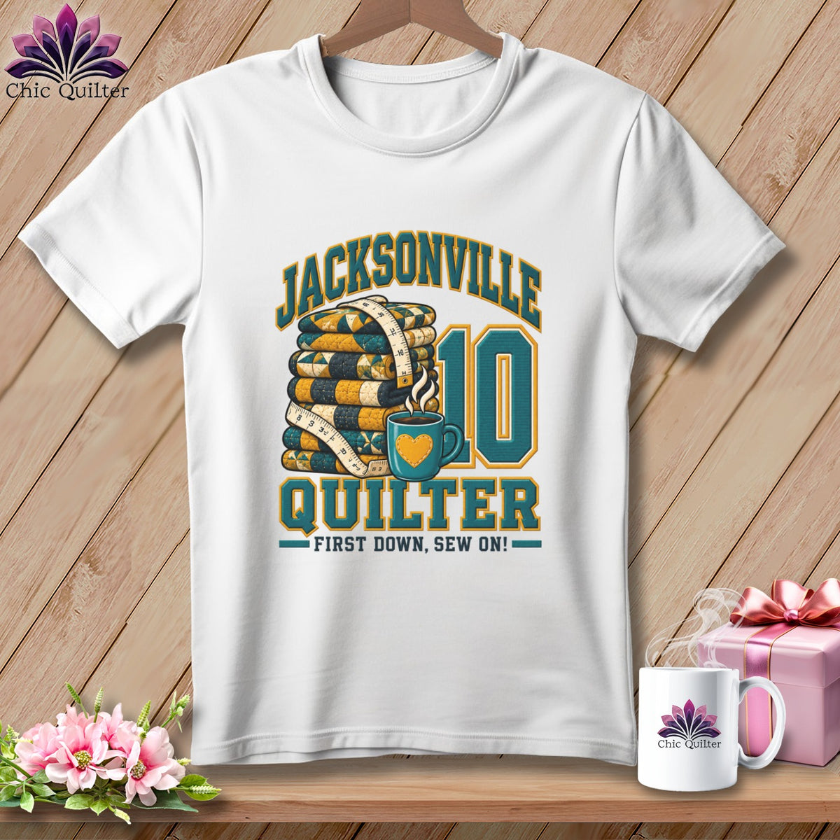 A white t-shirt features a Jacksonville Quilter graphic with a folded quilt stack, measuring tape, and coffee mug.
