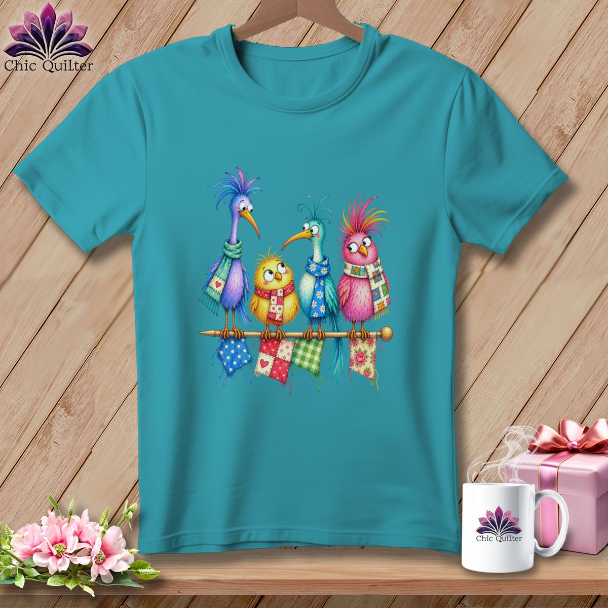 Teal t-shirt featuring a cartoon graphic of four colorful birds wearing scarves on a wooden background.