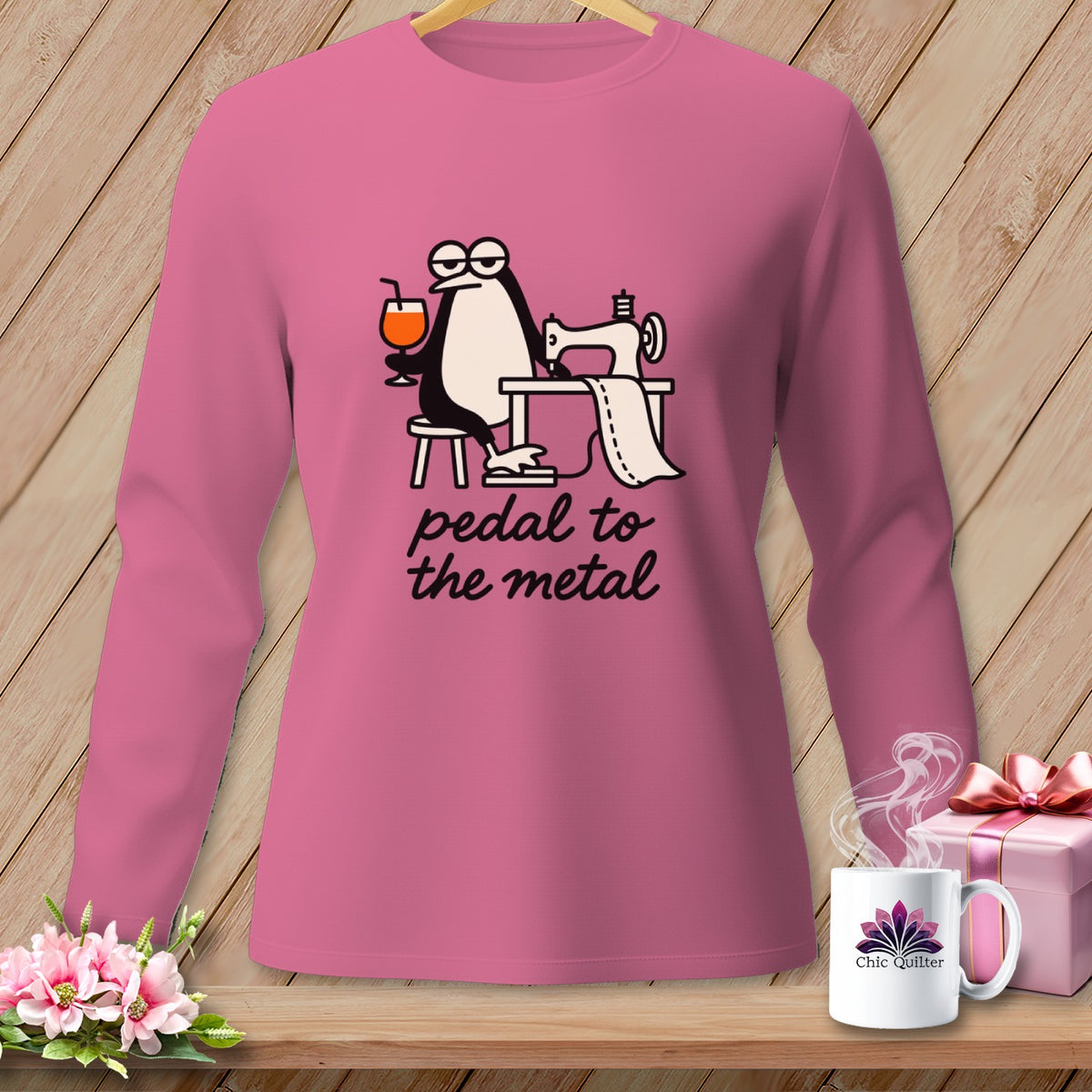 Pink shirt with a penguin at a sewing machine, holding a drink, with text "pedal to the metal."