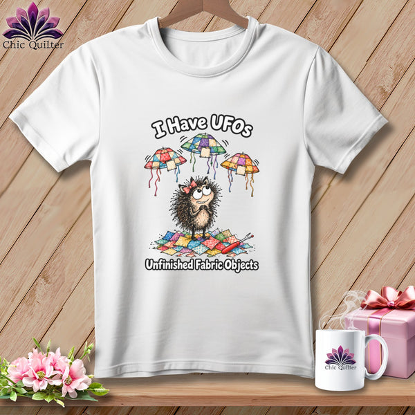 White t-shirt featuring a cartoon hedgehog graphic with patchwork UFOs and the text I Have UFOs Unfinished Fabric Objects.
