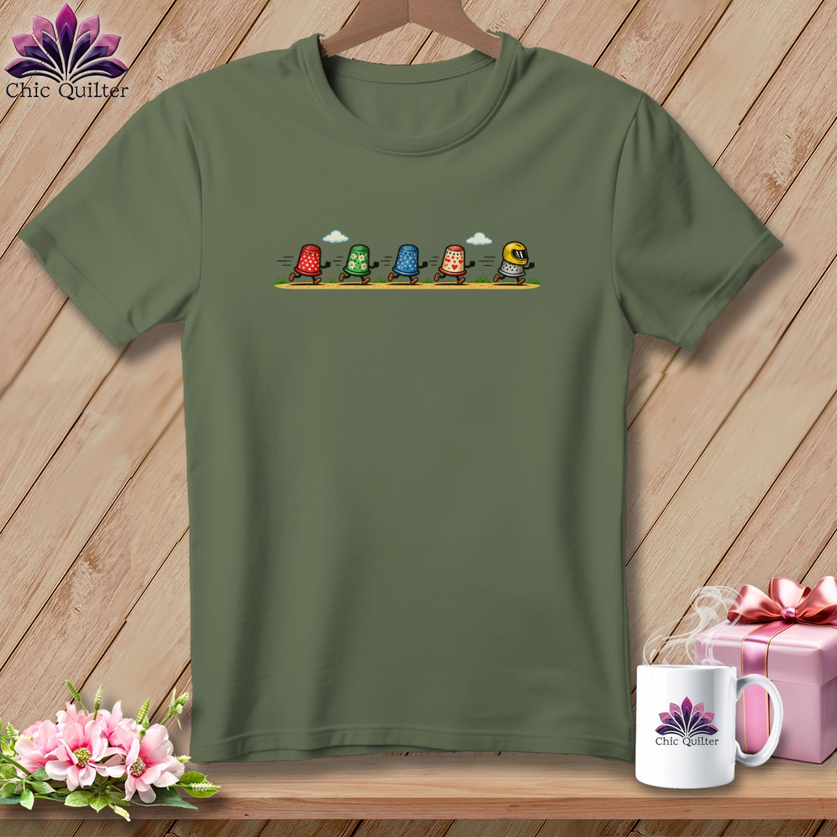 An olive green t-shirt with a graphic of five animated thimbles running across a path.