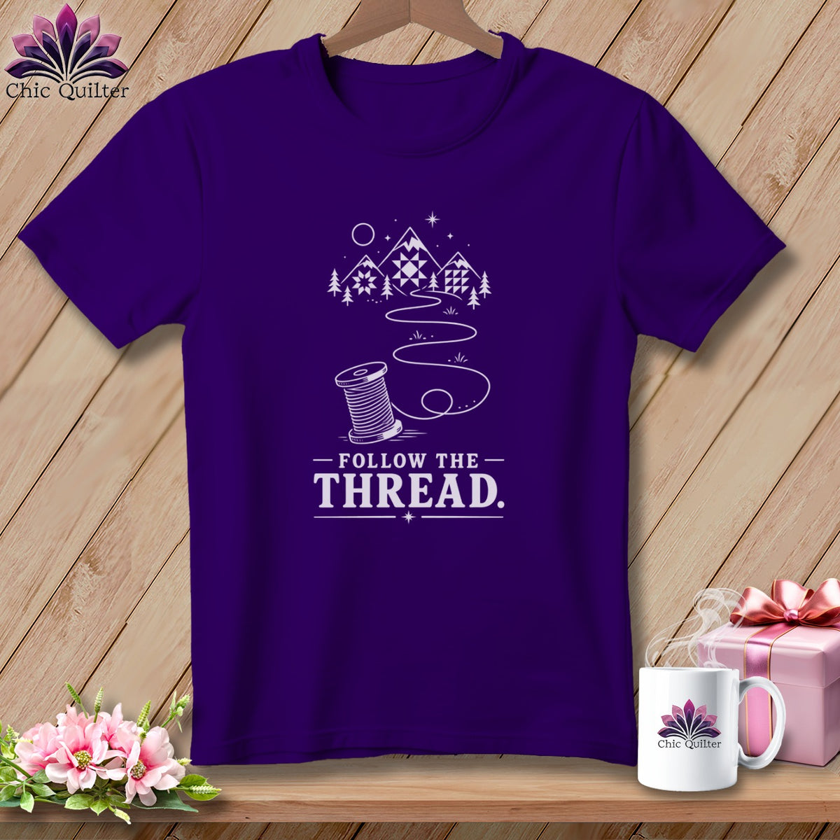 Purple t-shirt with mountains, trees, and a spool of thread design, reading "Follow the Thread."