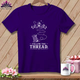 Purple t-shirt with mountains, trees, and a spool of thread design, reading 