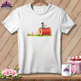 A white short-sleeved t-shirt features a graphic of a woman riding on a large red spool of thread.