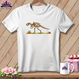 White t-shirt featuring a cartoon dinosaur skeleton wearing a patchwork quilt and pulling a thread spool.