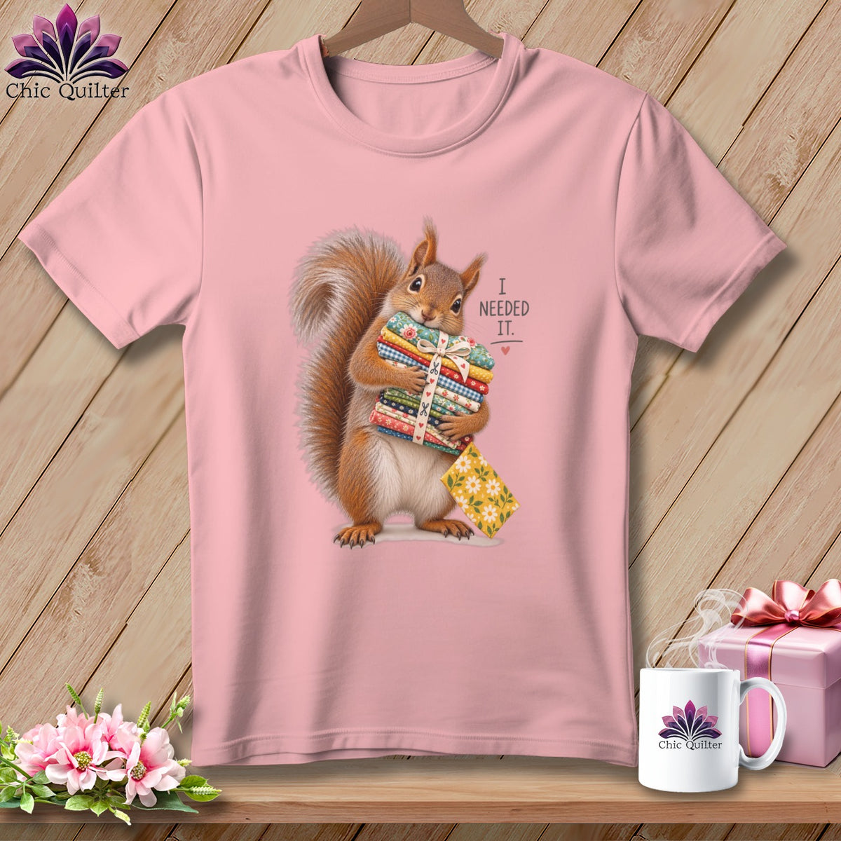 Squirrel holding fabric stacks with "I NEEDED IT." text on pink t-shirt.
