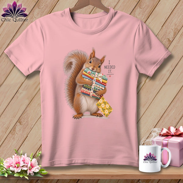 Squirrel holding fabric stacks with "I NEEDED IT." text on pink t-shirt.