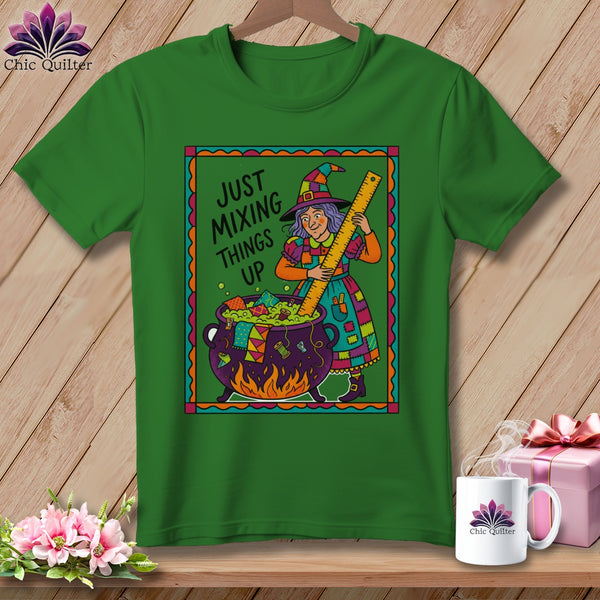 Green t-shirt with cartoon witch stirring cauldron of quilt scraps, text "Just Mixing Things Up".
