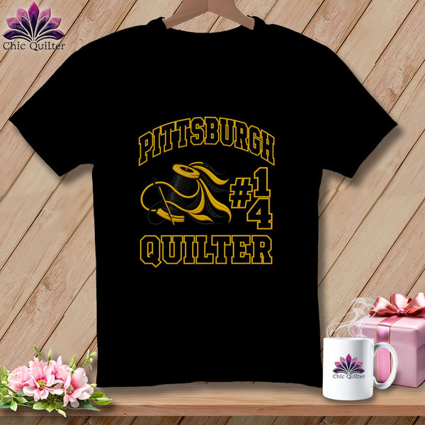 A black t-shirt featuring yellow text that reads Pittsburgh Quilter, with a spool of thread.