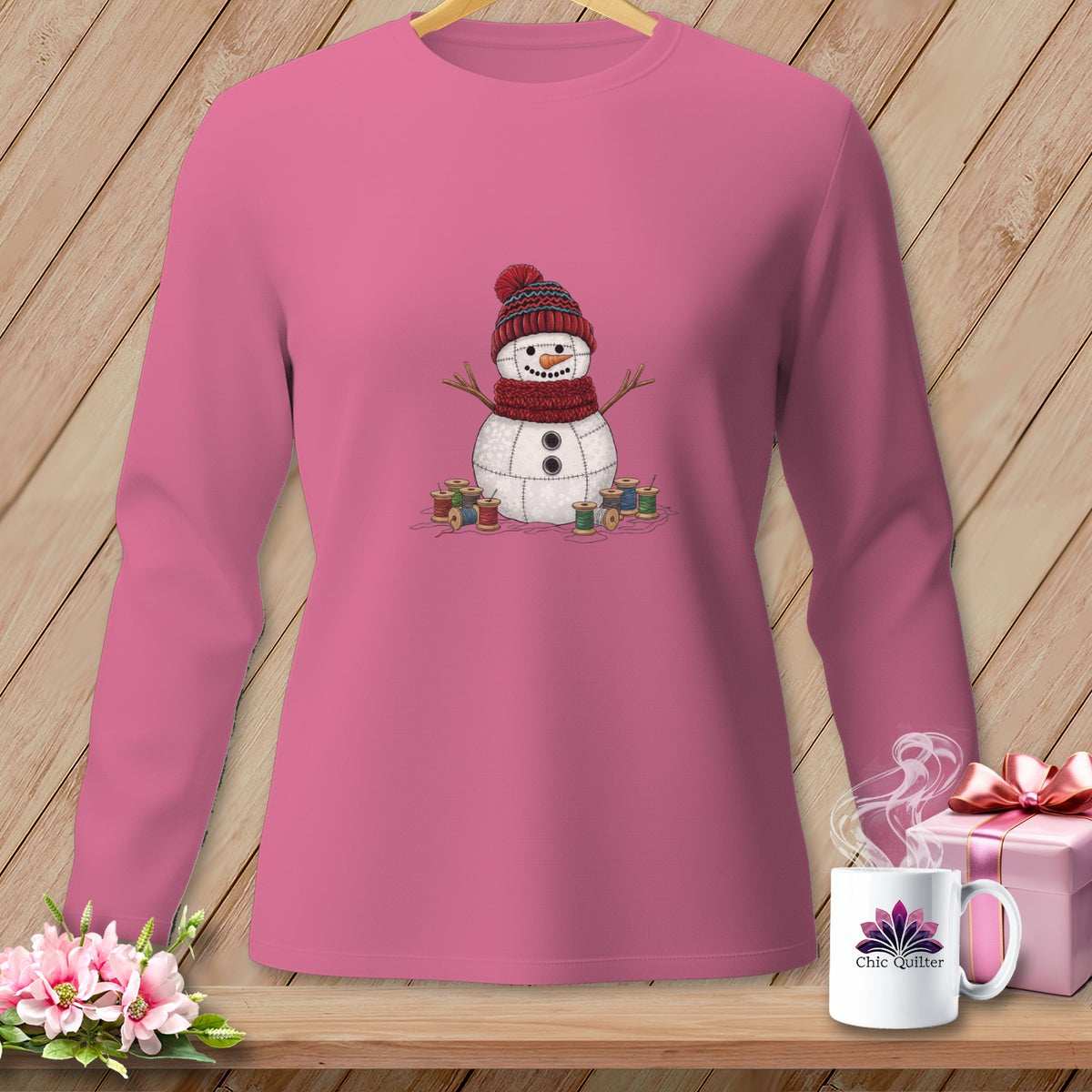 Pink long-sleeve shirt with a stitched snowman wearing a hat and scarf, surrounded by spools of thread.