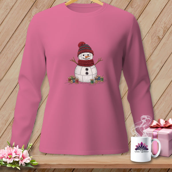 Pink long-sleeve shirt with a stitched snowman wearing a hat and scarf, surrounded by spools of thread.