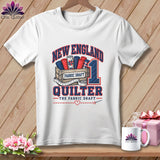 White t-shirt featuring New England Quilter graphic with fabric rolls, measuring tape, and text.