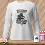 A white long-sleeved shirt featuring a graphic of a bear sitting on quilts with the text QUILT YOUR OWN DAMN QUILT.