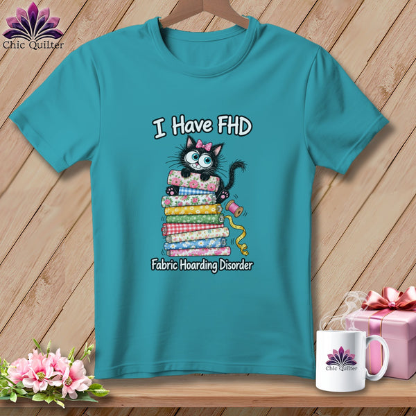 A turquoise t-shirt with a cartoon cat on a stack of fabric and text reading I Have FHD Fabric Hoarding Disorder.
