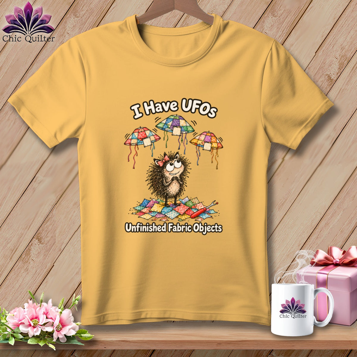 A yellow t-shirt hanging on a wooden background, featuring a cute hedgehog cartoon graphic with the text I Have UFOs Unfinished Fabric Objects.