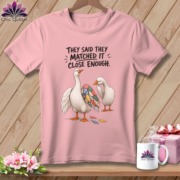 Pink t-shirt with two geese, one with a patchwork wing, and text "They said they matched it = close enough."