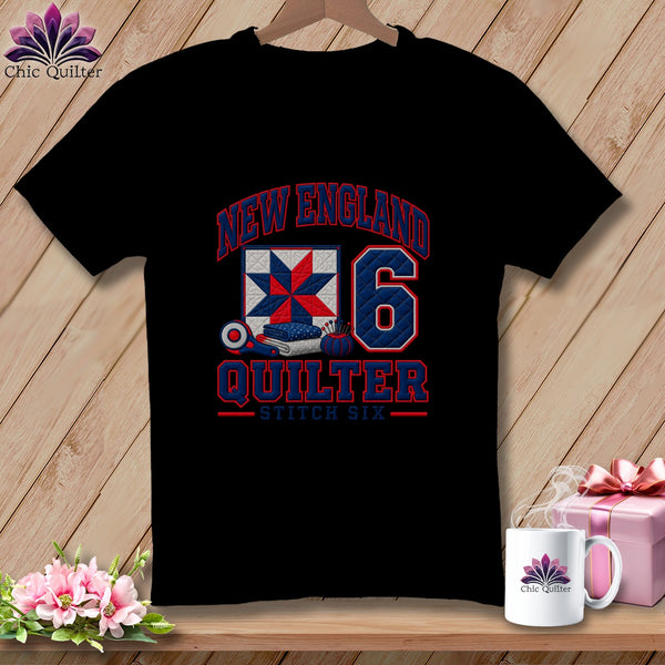A black t-shirt featuring a New England Quilter graphic with a quilt block, number six, and sewing tools.
