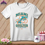 A white t-shirt features a dolphin graphic with the text MIAMI QUILTER against a wooden background.