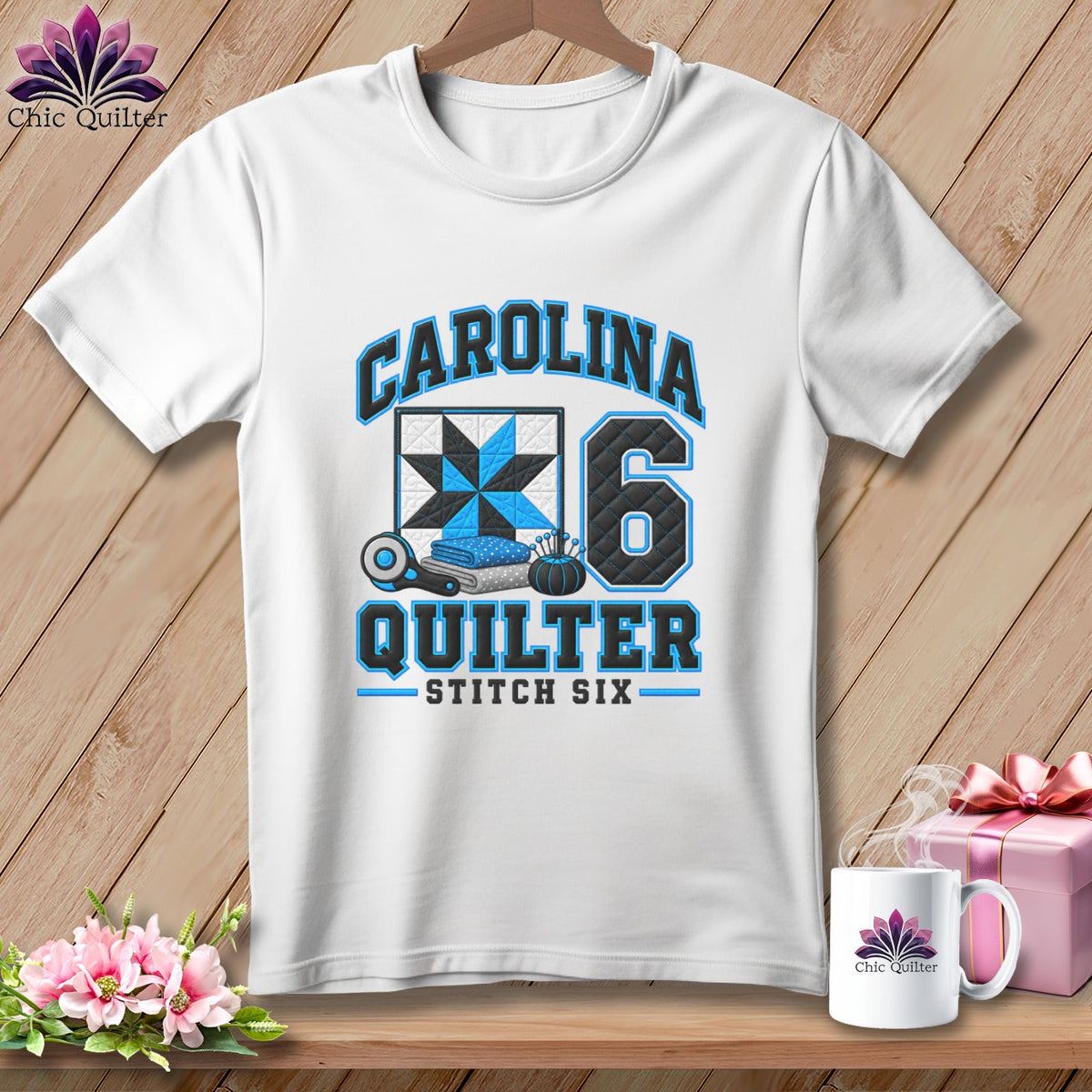 A white t-shirt hanging on a wooden background features blue and black quilting text and graphics.