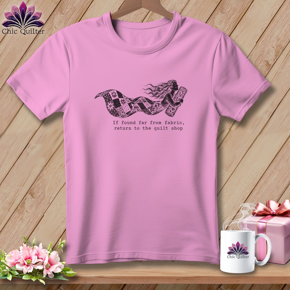 Pink t-shirt with a graphic of a woman wrapped in a quilt, text reads "If found far from fabric, return to the quilt shop".