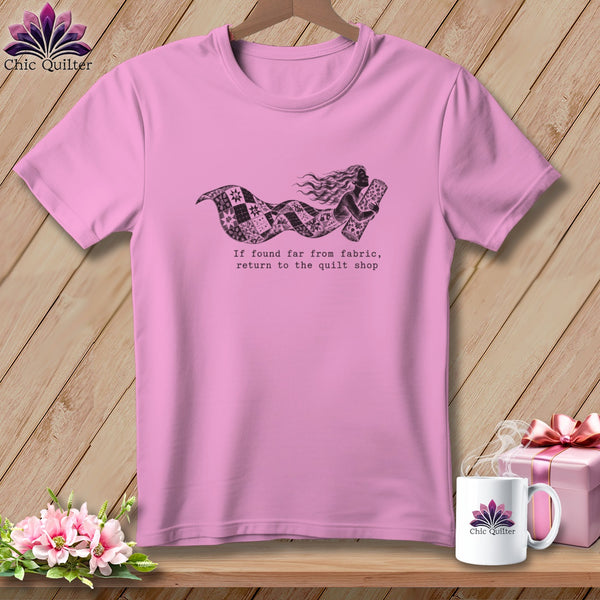 Pink t-shirt with a graphic of a woman wrapped in a quilt, text reads "If found far from fabric, return to the quilt shop".