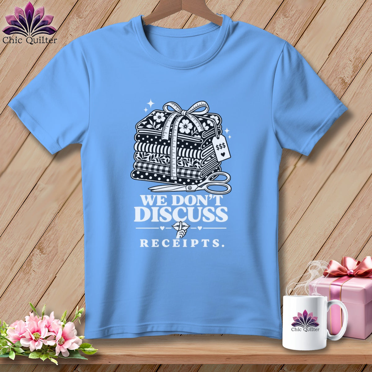 Light blue t-shirt with graphic of stacked fabric, scissors, and text "WE DON'T DISCUSS RECEIPTS."