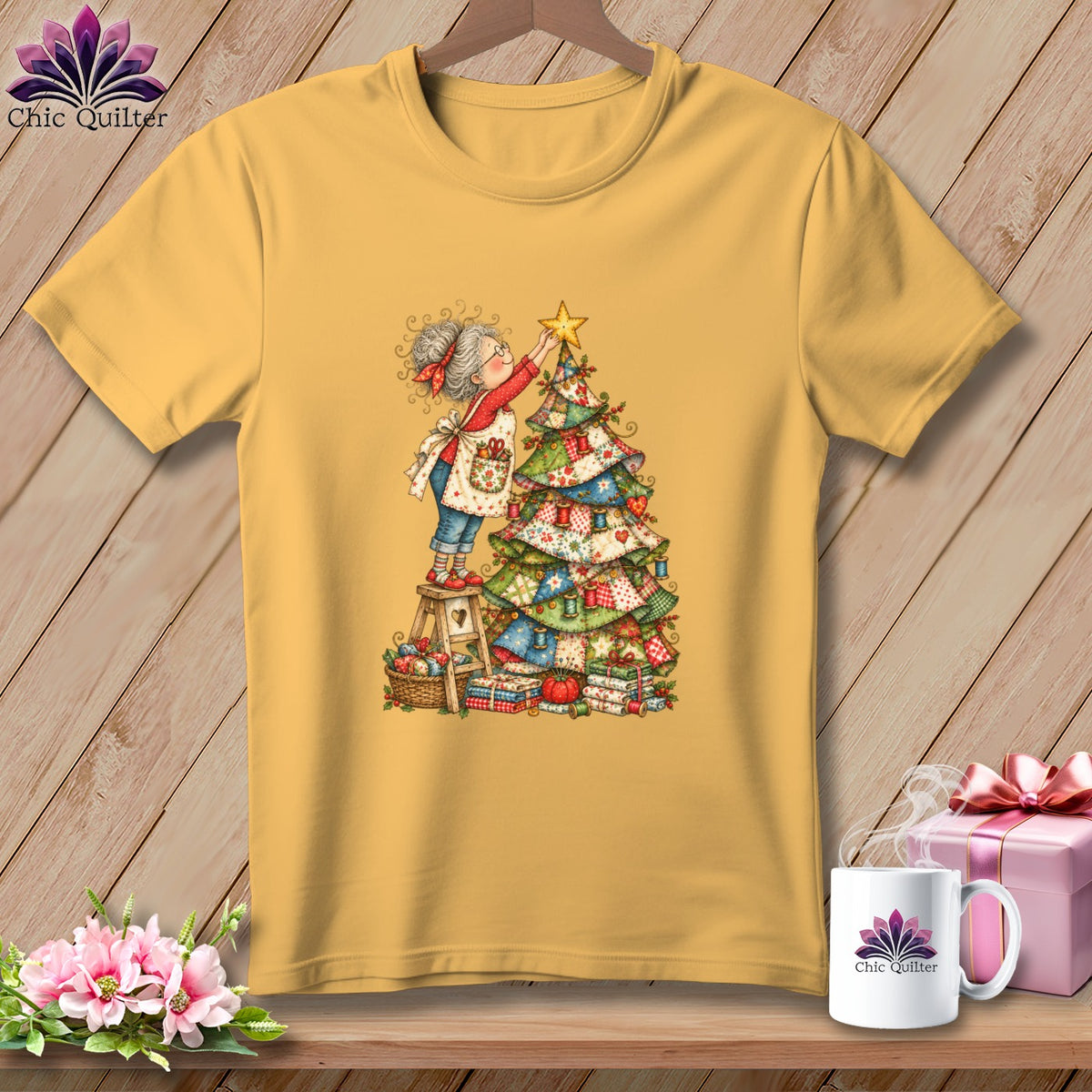 A mustard yellow t-shirt features a whimsical illustration of a woman placing a star on a quilted Christmas tree.